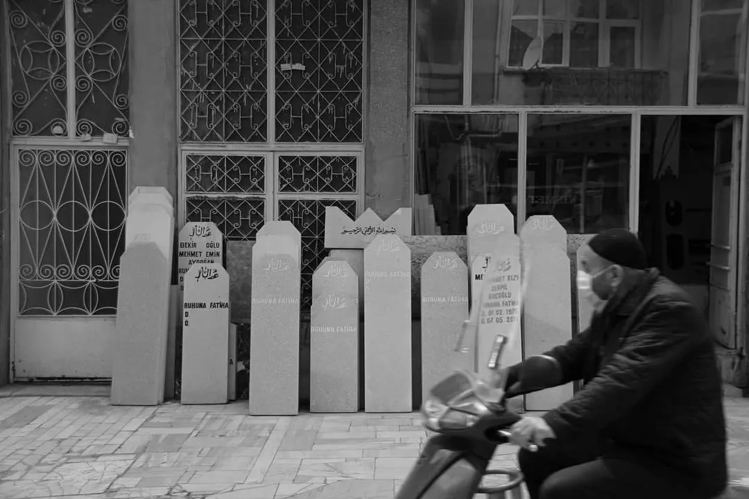 Dükkân önüne dizilmiş mezar taşlarının yanından geçen motosikletli